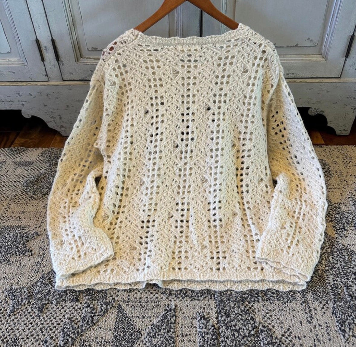 Beige crochet sweater on a wooden hanger against a rustic background