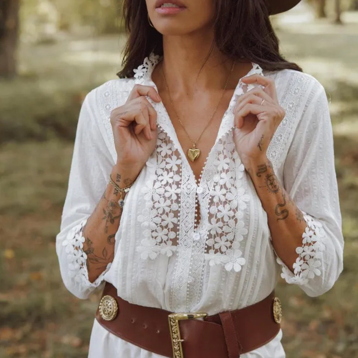 Woman wearing a white lace blouse with a brown belt in an outdoor setting