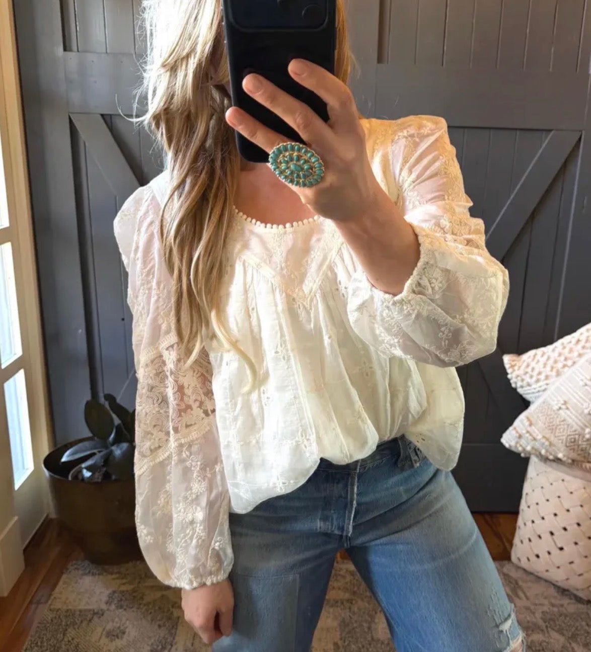 Person wearing a white lace top and blue jeans taking a mirror selfie.