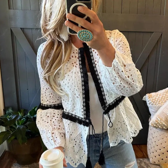 Person wearing a white lace top with black trim, holding a coffee cup indoors.