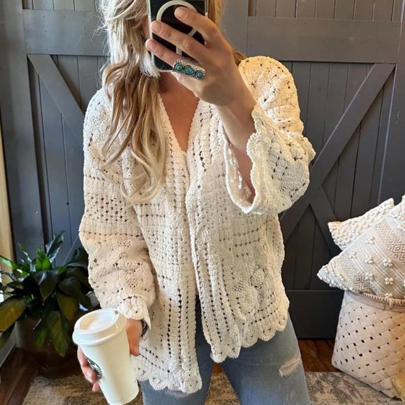 Woman wearing a beige crochet cardigan holding a coffee cup indoors.