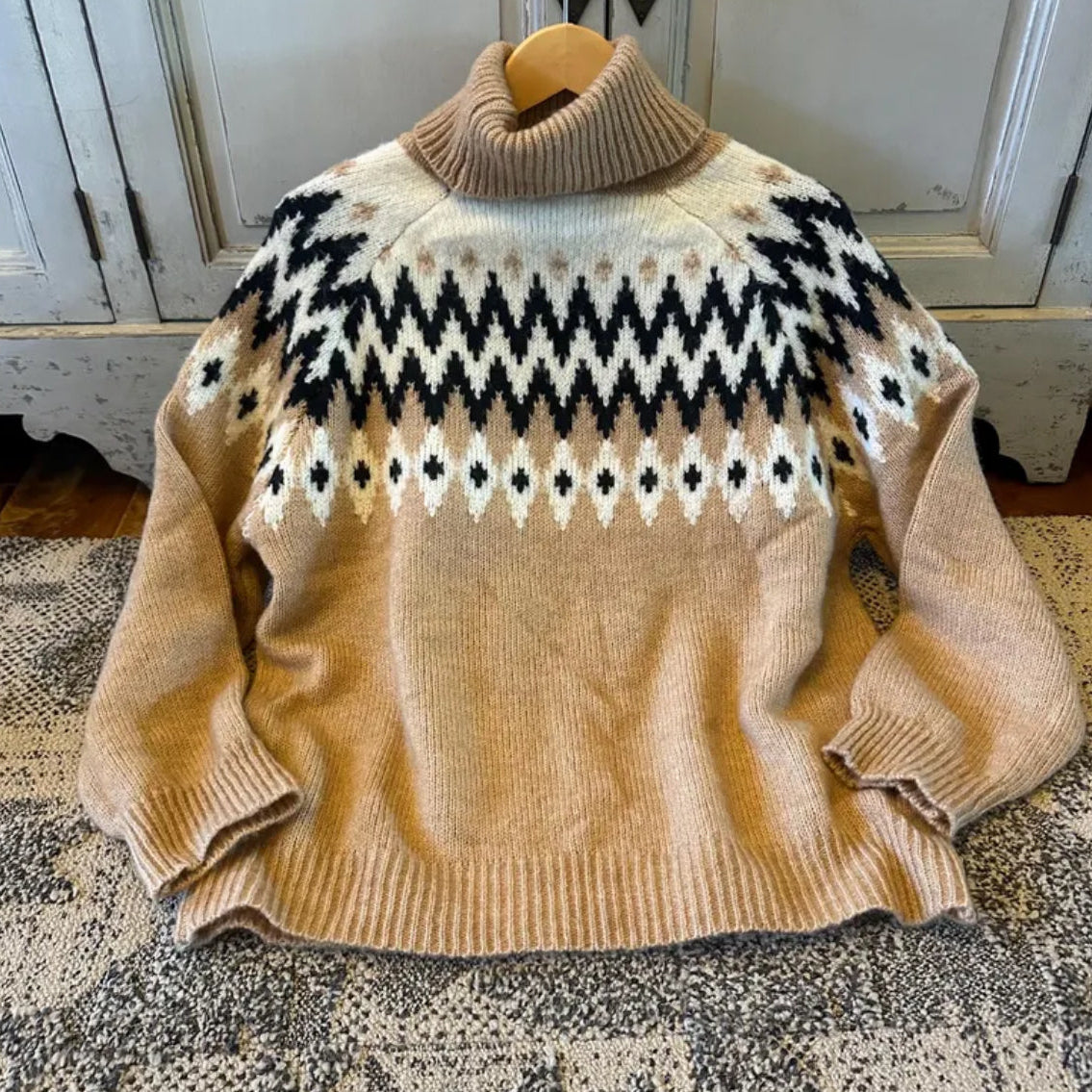 Beige sweater with a pattern on a hanger against a neutral background