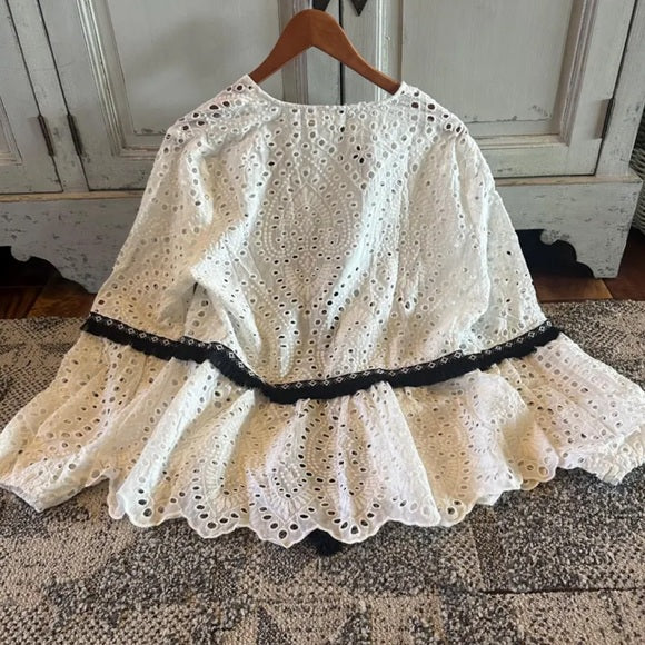 White lace blouse with black trim on a wooden hanger against a neutral background