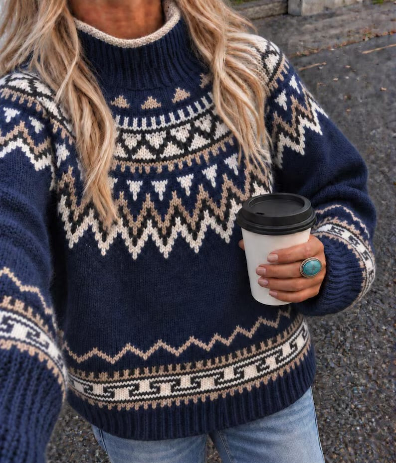 A woman wearing a navy blue knit sweater with a cream and beige Fair Isle pattern, holding a white coffee cup with a black lid.