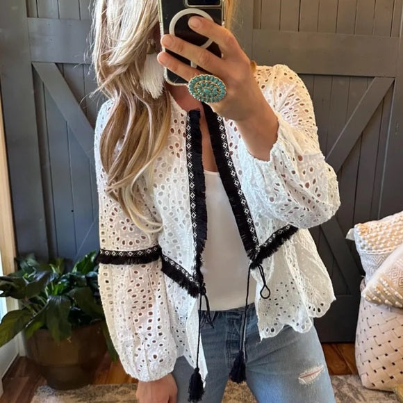 Model wearing a white lace cardigan with black trim, taking a mirror selfie.