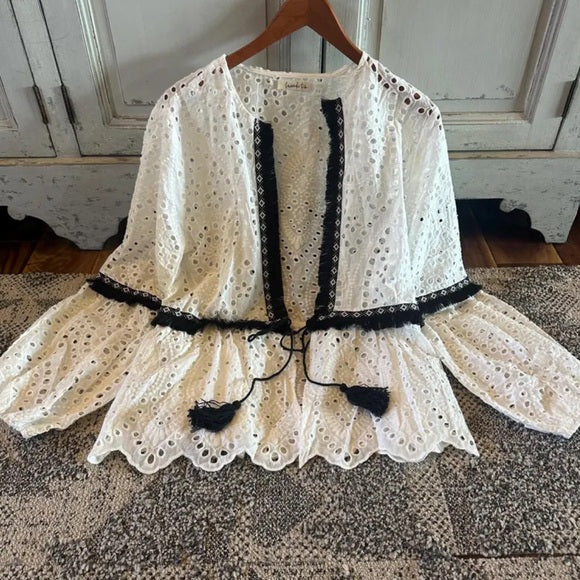 White lace top with black trim on a wooden hanger against a rustic background
