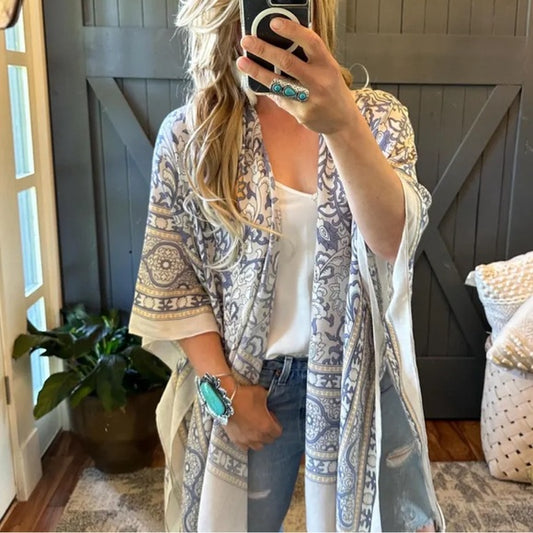 Woman wearing a patterned kimono over a white top and jeans, taking a mirror selfie.