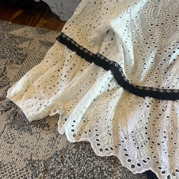 Close-up of a white lace blouse with black trim on a textured surface.