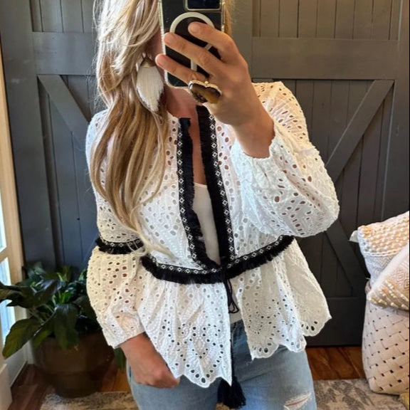 Person wearing a white lace top with black trim in a room with wooden doors and a plant.
