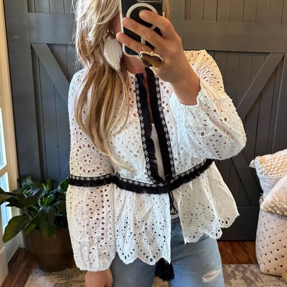 Western Model wearing a white lace top with black trim, standing indoors.