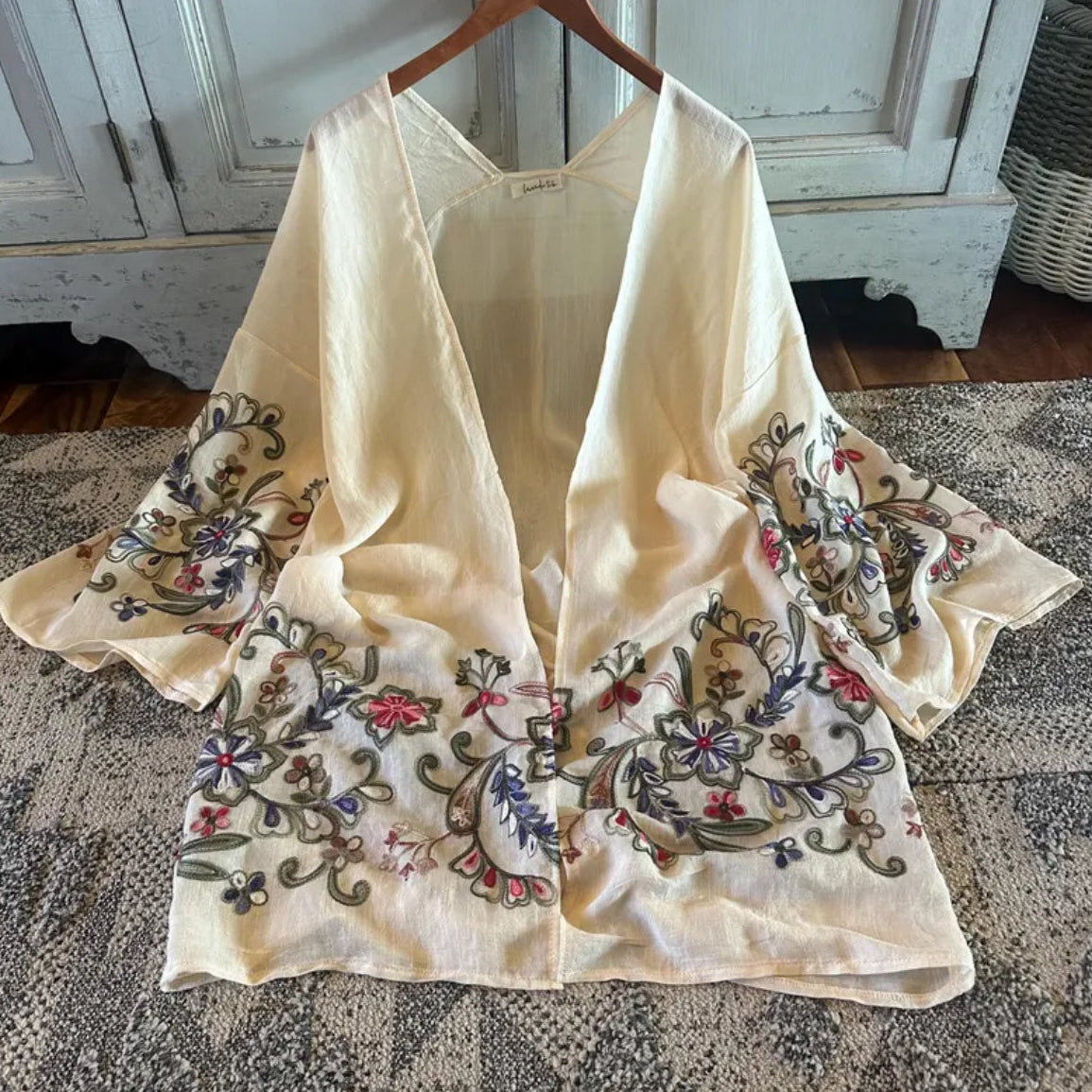 Embroidered beige scarf on a wooden hanger against a rustic background