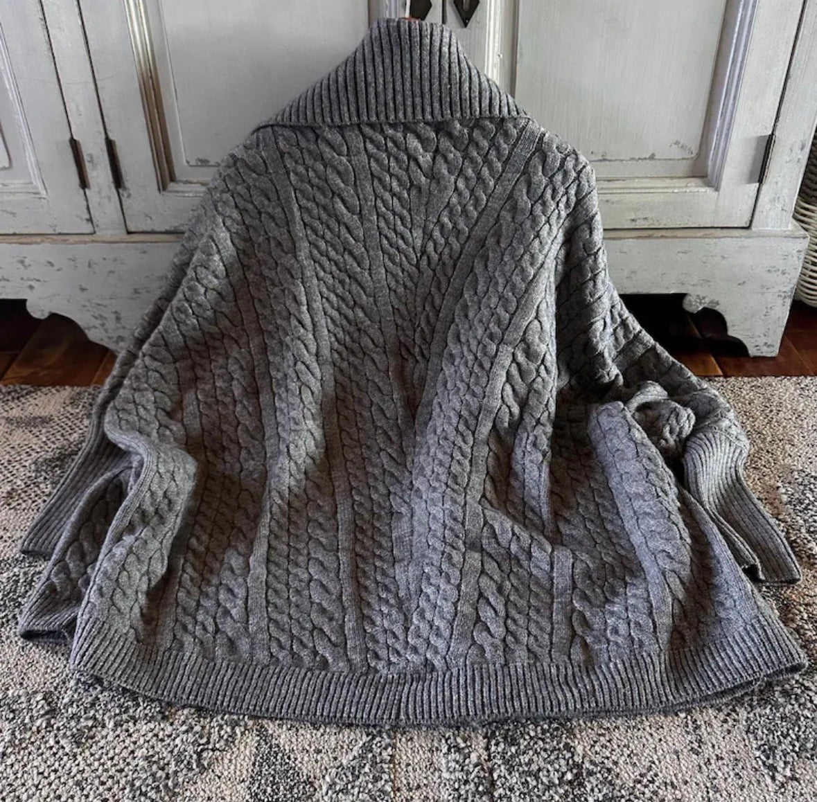 Gray cable knit sweater draped over a chair in a room with wooden floors and white walls.