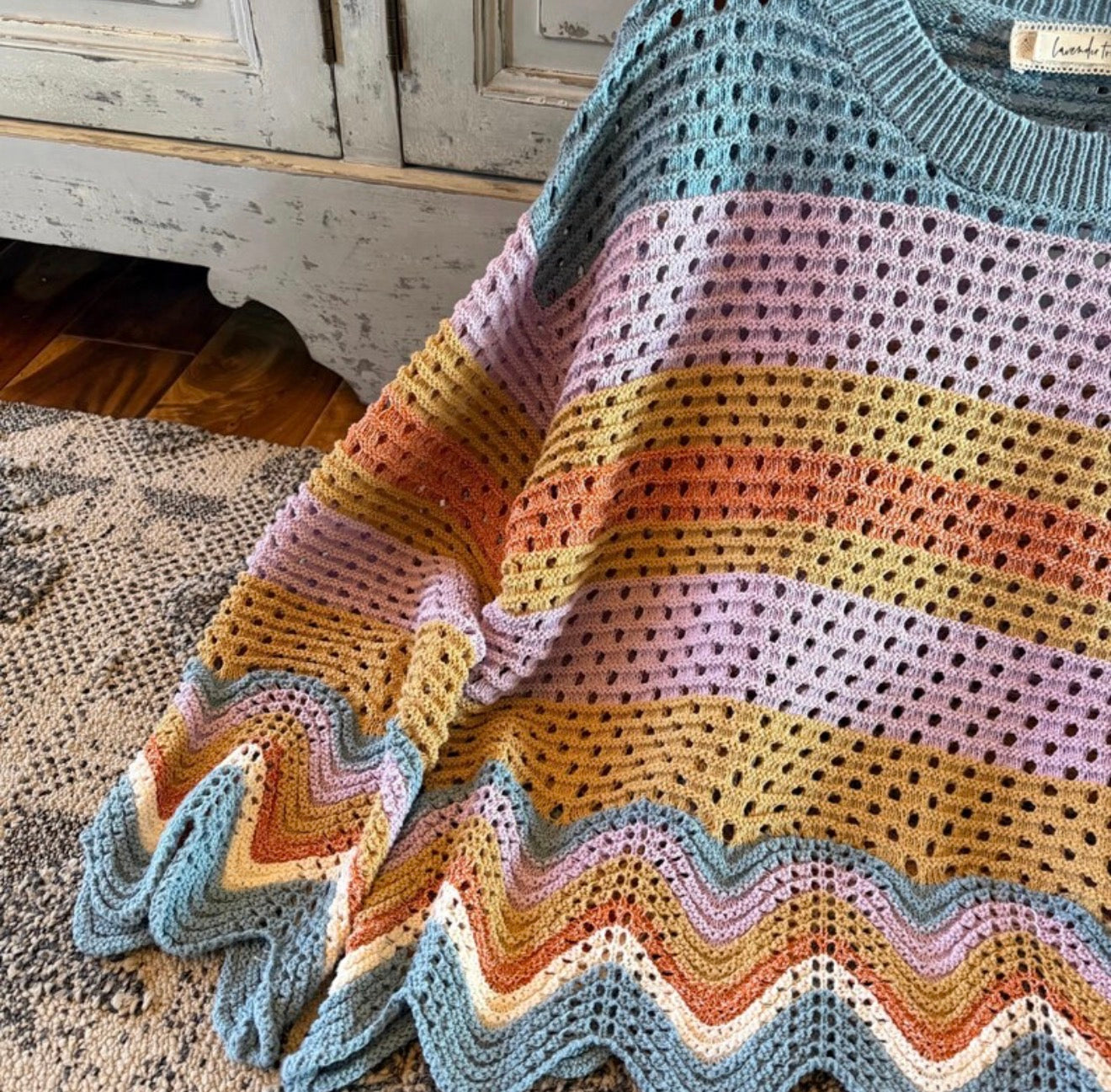 Colorful crocheted blanket with a wavy edge on a wooden floor.
