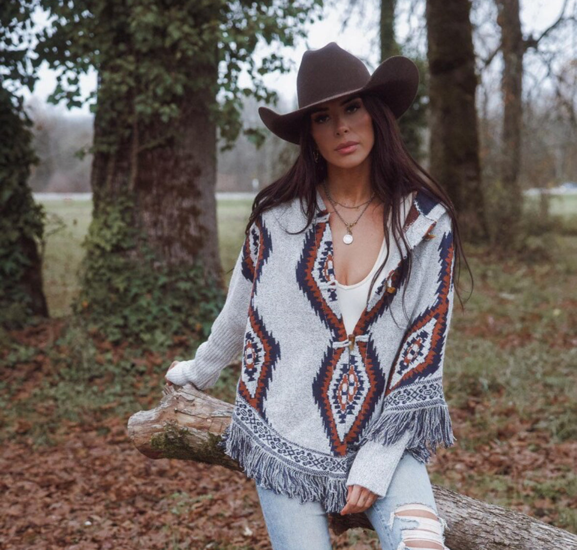 Woman wearing a patterned cardigan and cowboy hat in a forest setting