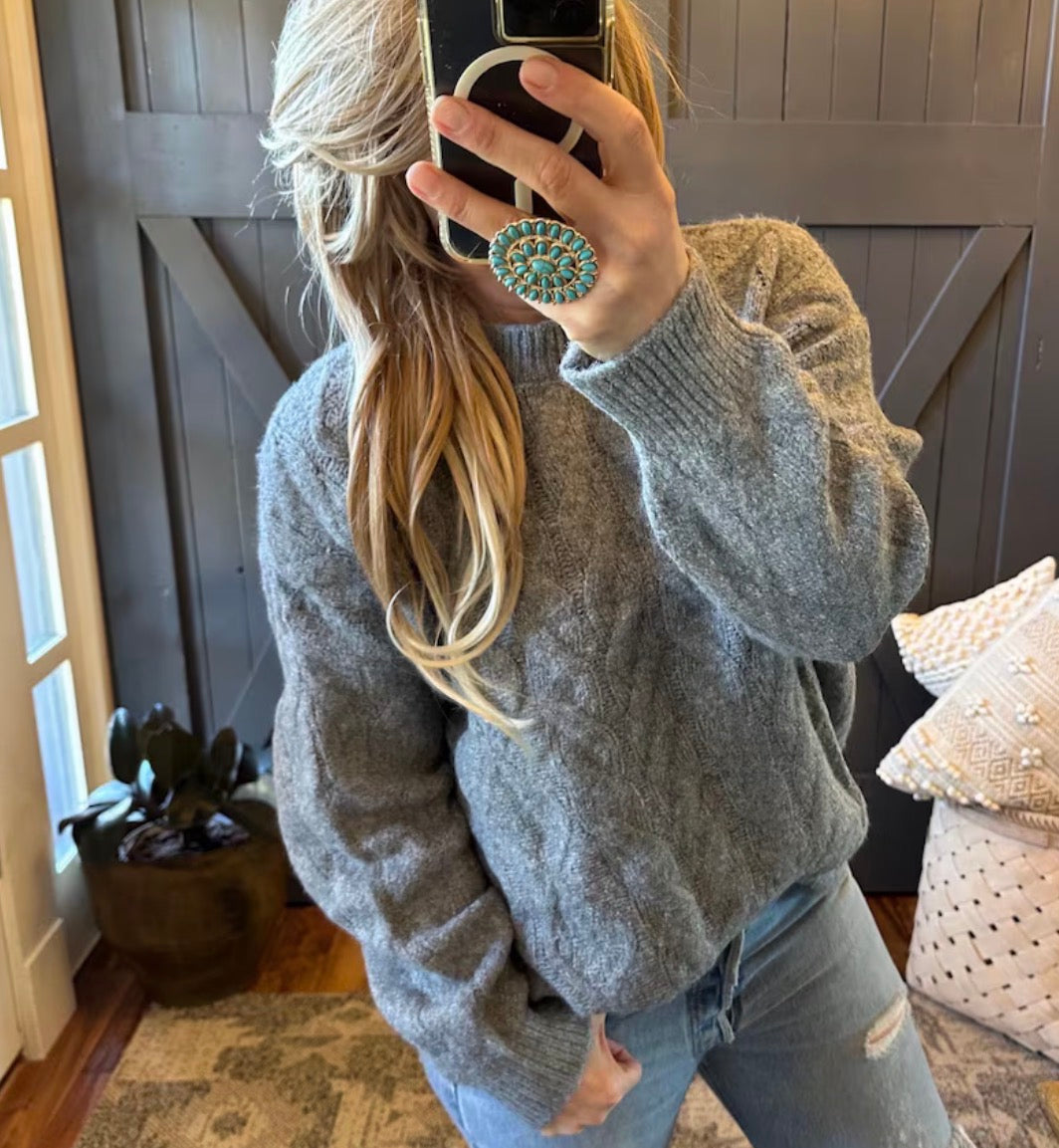 Person wearing a gray sweater and jeans, taking a mirror selfie.