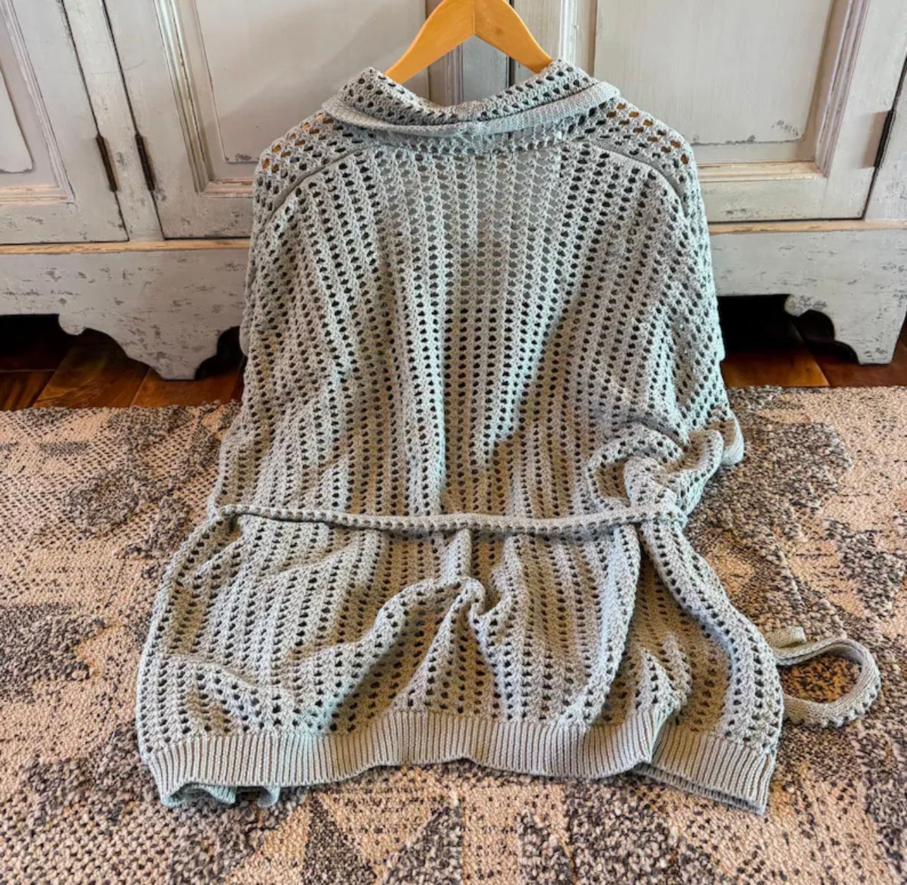 Knitted poncho on a wooden hanger against a rustic wooden door background