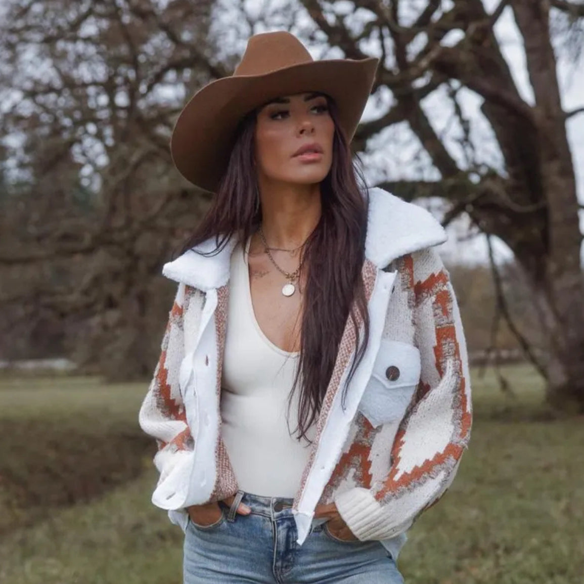 Woman wearing a brown hat, patterned coat, and jeans outdoors.