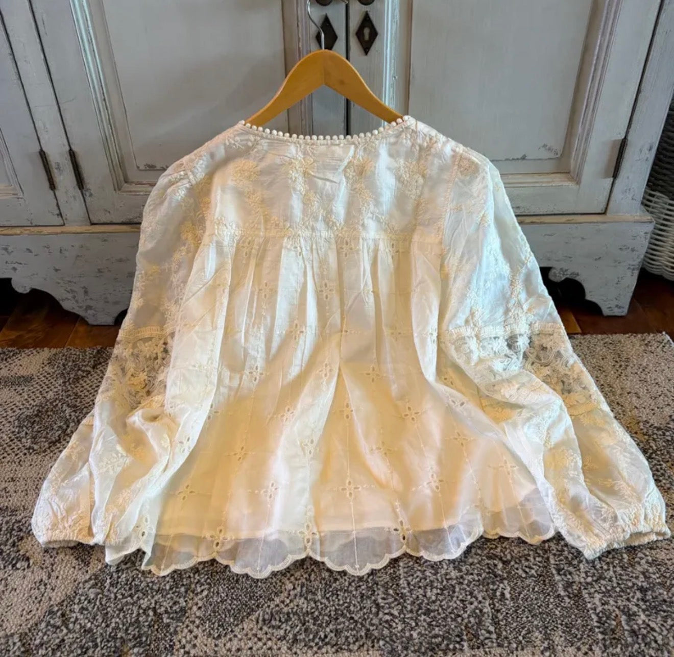 White lace blouse on a wooden hanger against a neutral background