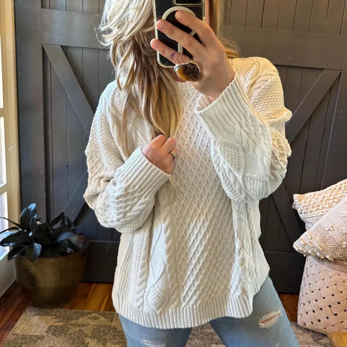 Person wearing a white cable knit sweater taking a mirror selfie.