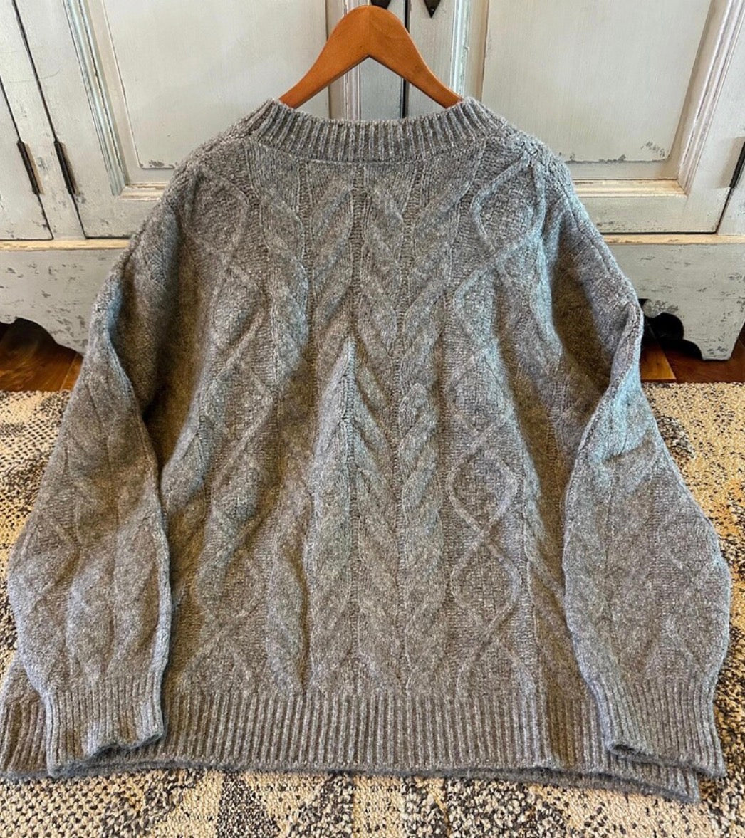Gray cable knit sweater on a wooden hanger against a white wall.