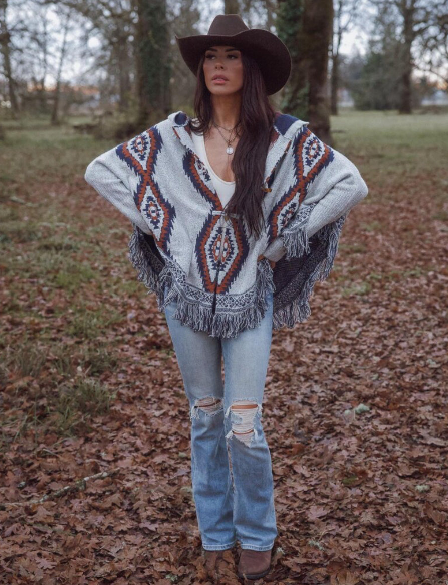 Woman wearing a patterned poncho and cowboy hat in a forest setting