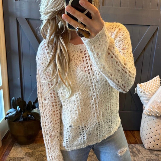 Person wearing a white crochet sweater and jeans, taking a mirror selfie.