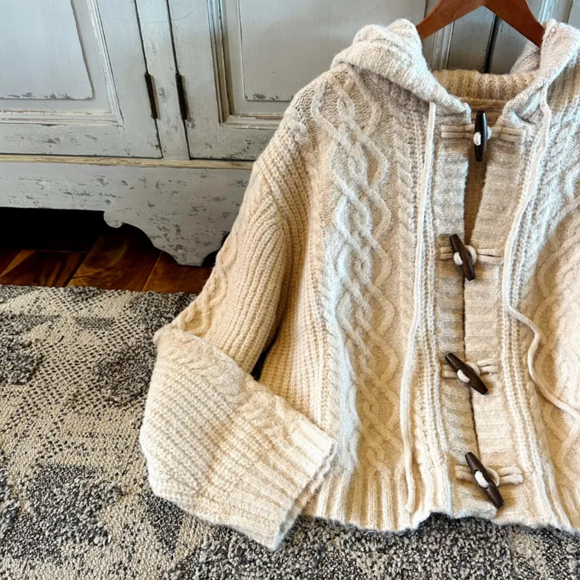 Beige cable knit cardigan with wooden buttons on a textured surface.