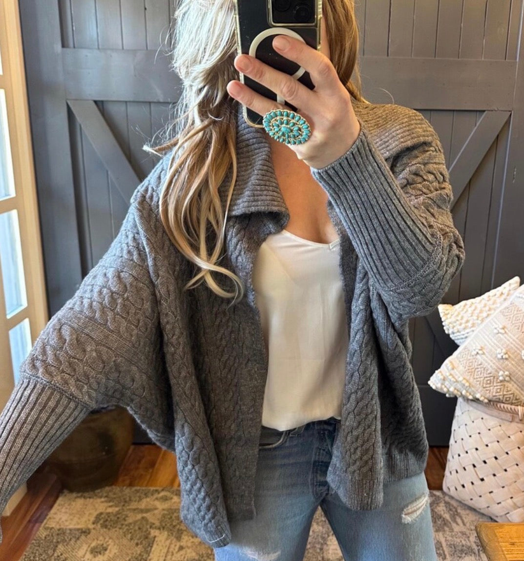 Person wearing a gray cable knit cardigan in a home setting