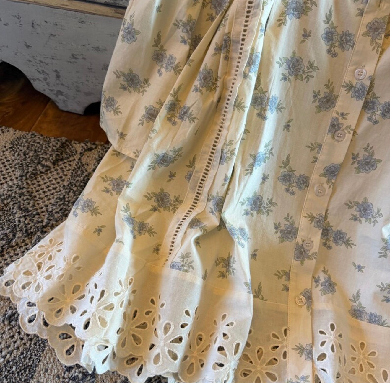 Floral patterned fabric with eyelet trim on a wooden floor.