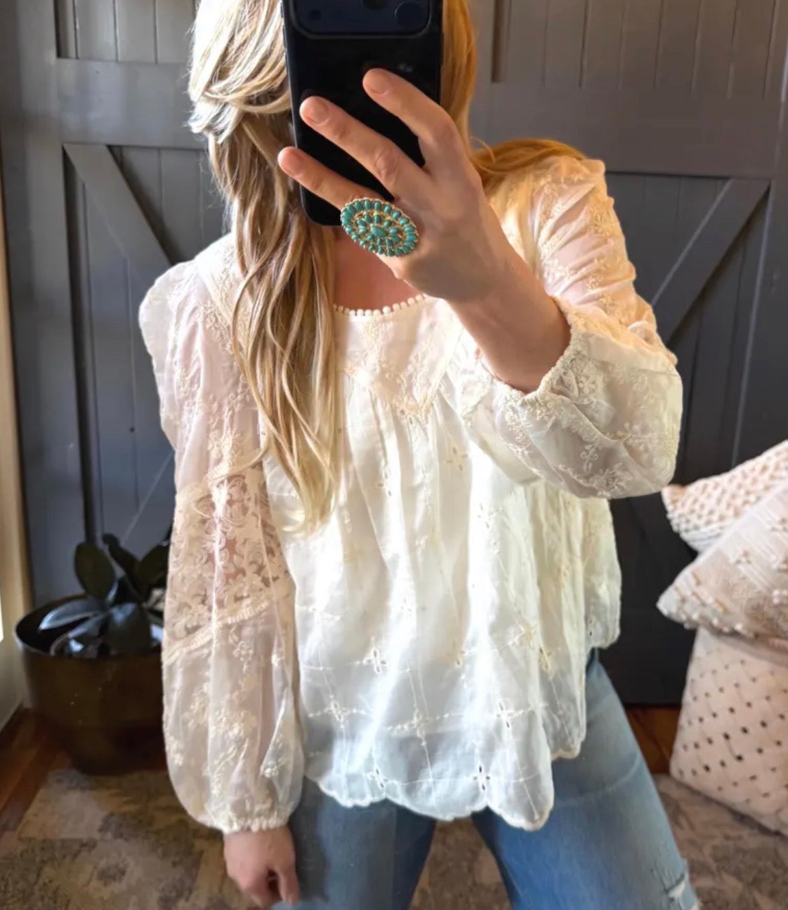 Person wearing a white lace top and blue jeans, holding a phone with a green case.