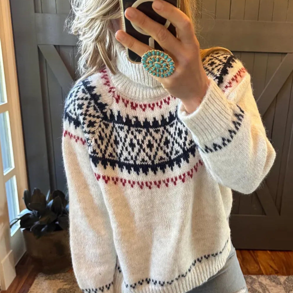 Person wearing a patterned sweater taking a mirror selfie indoors.