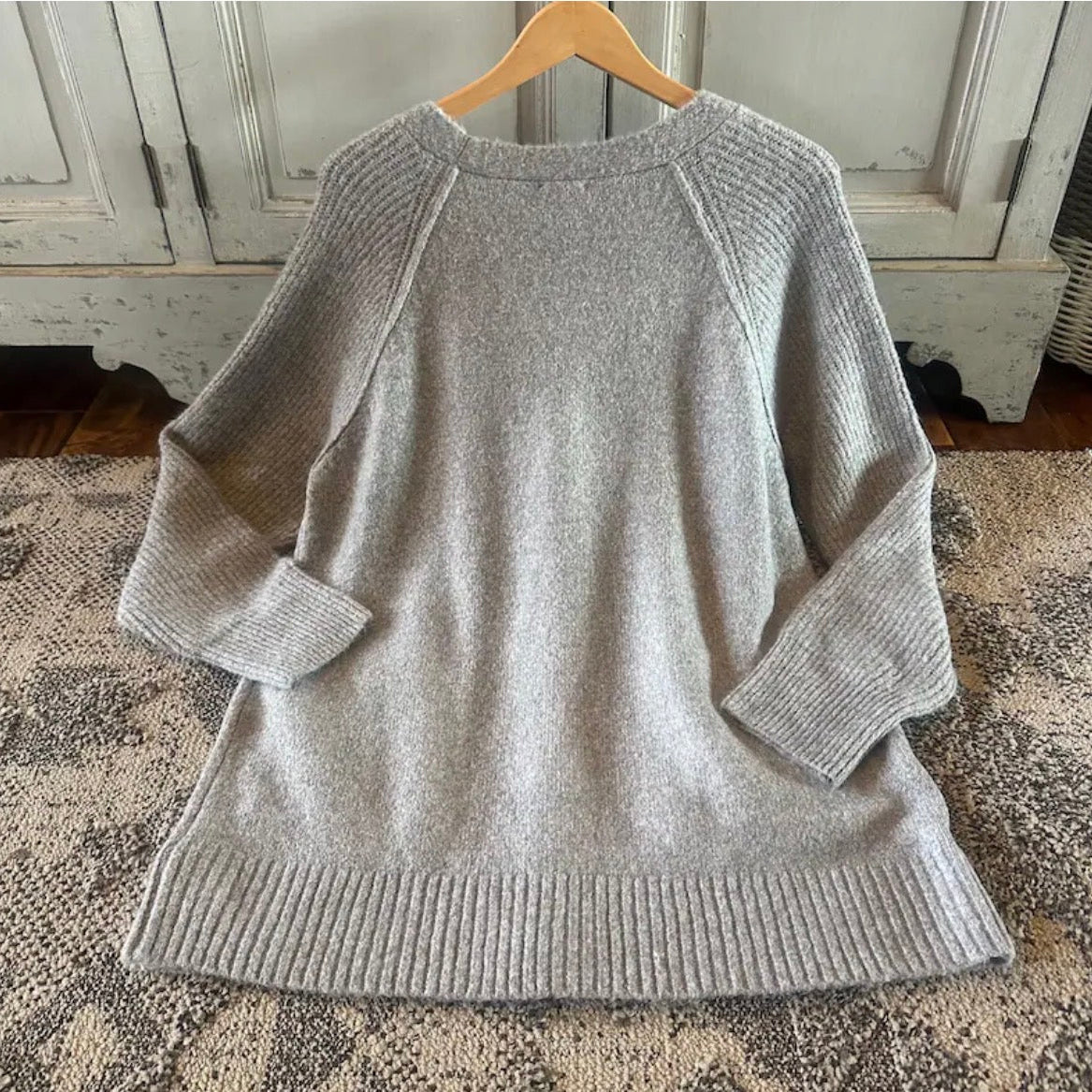 Gray sweater on a wooden hanger against a rustic wooden cabinet background