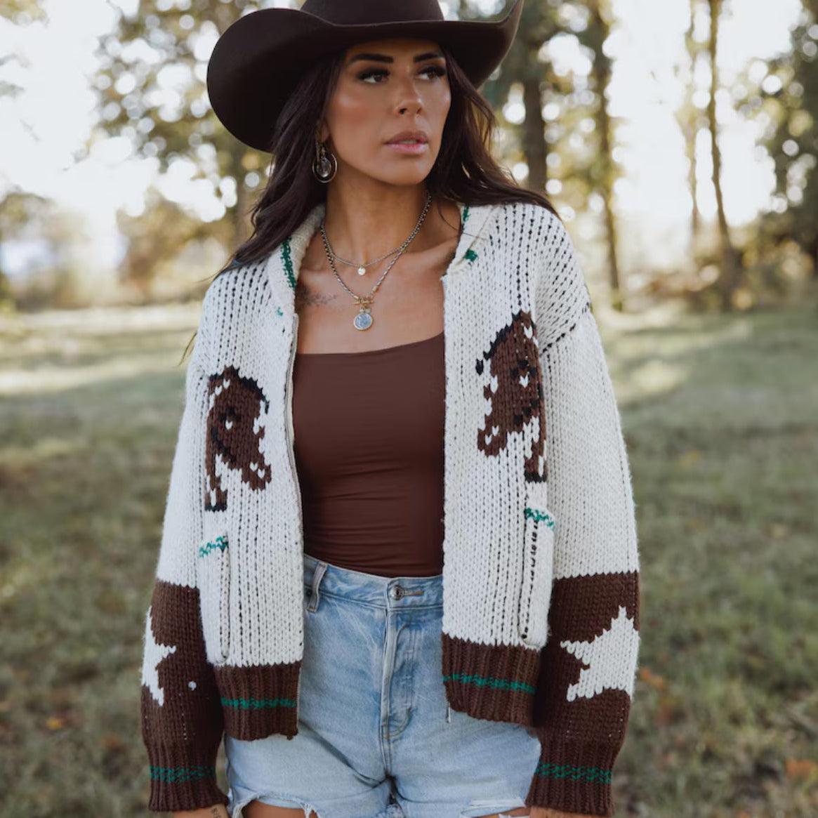 Woman wearing a patterned cardigan with horse designs outdoors.