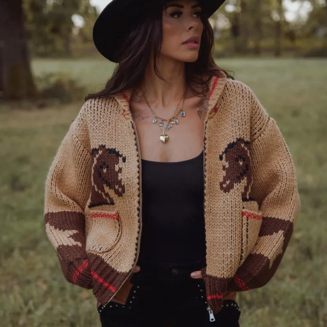 Woman wearing a beige cardigan with horse patterns in a grassy field