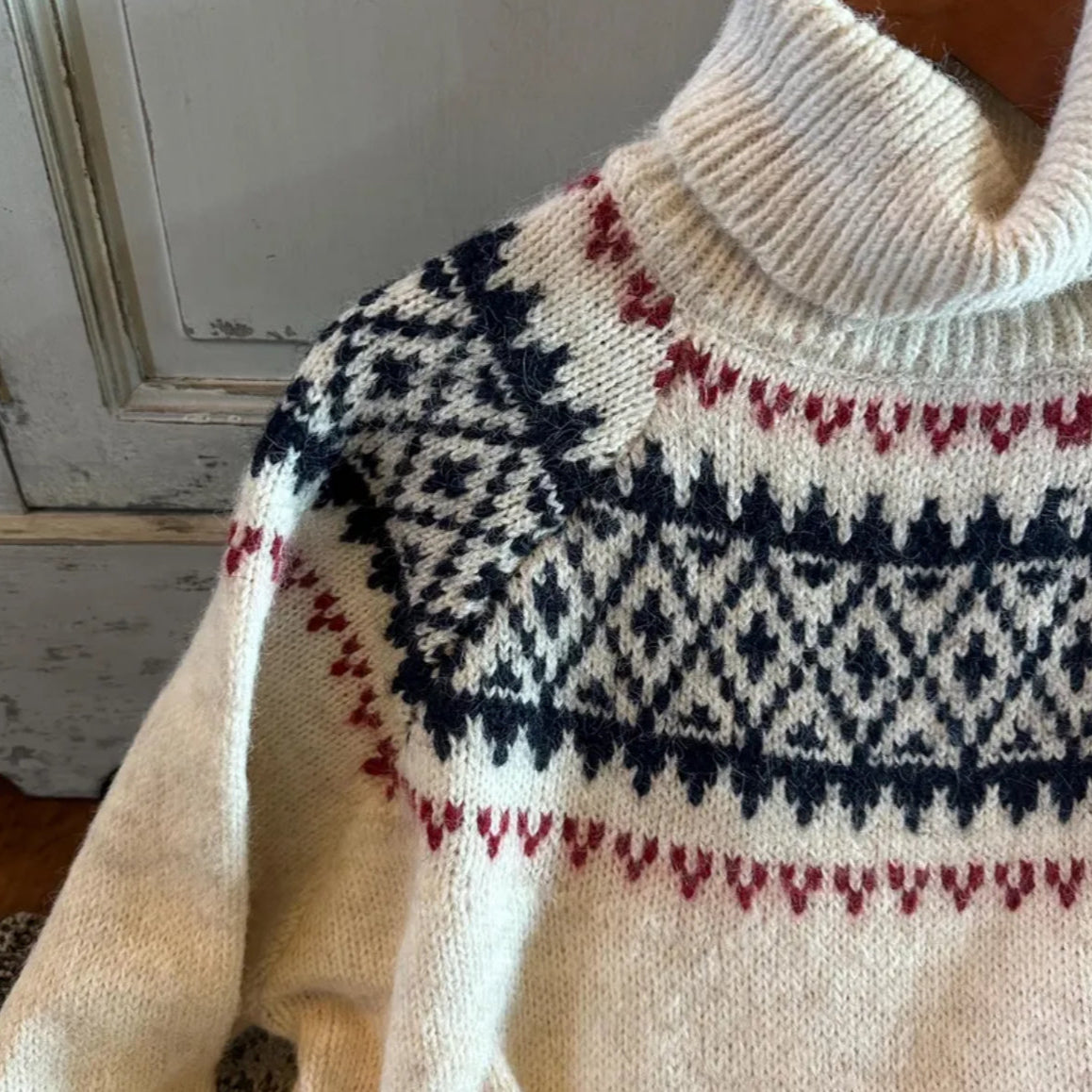 Close-up of a cream-colored sweater with a patterned design against a neutral background.