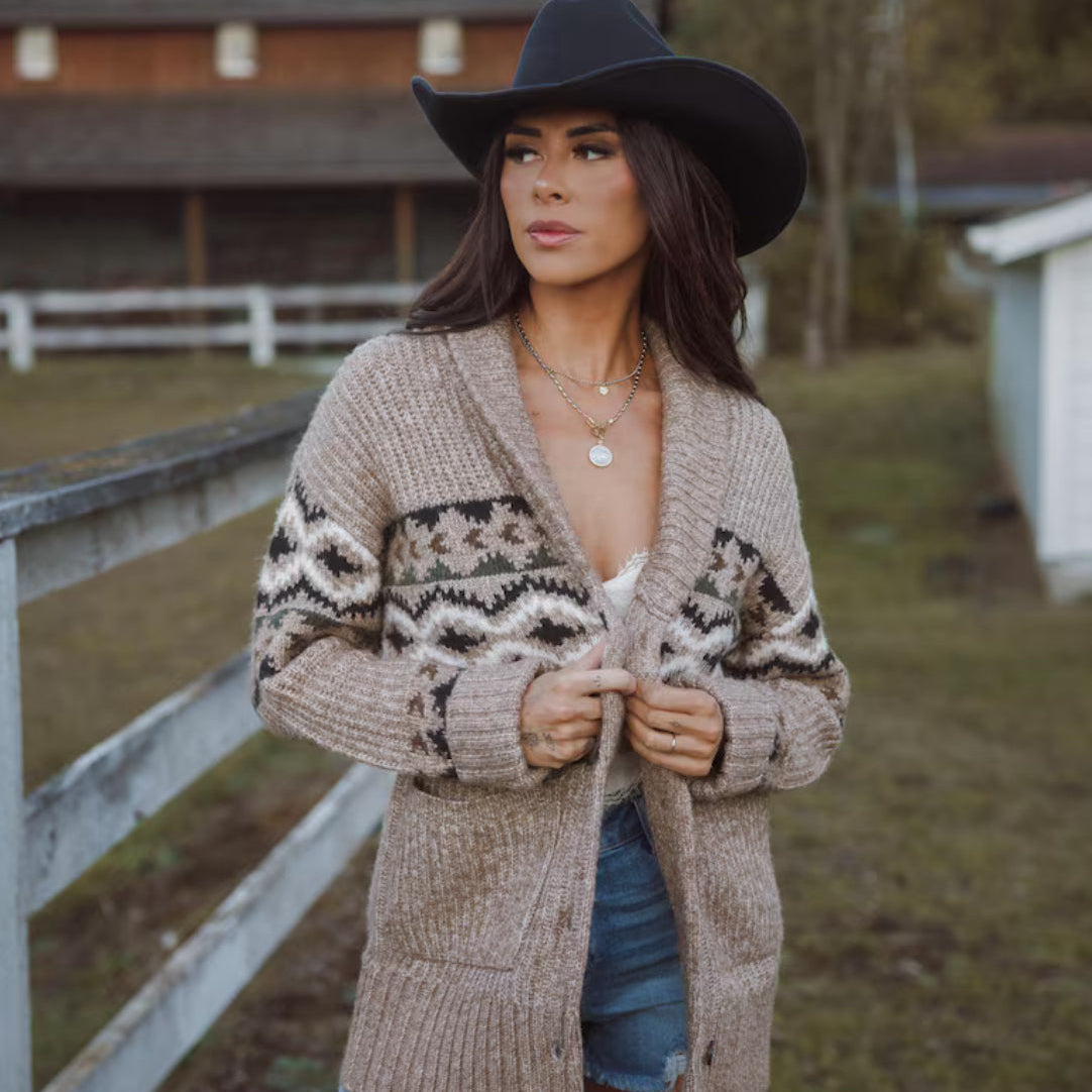 Woman wearing a patterned cardigan and cowboy hat in a rural setting