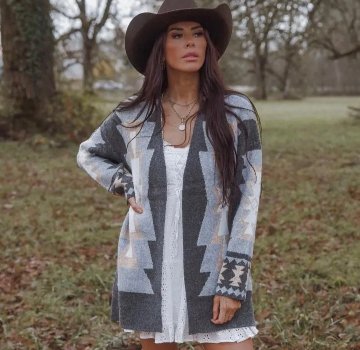 Woman wearing a patterned cardigan and hat in a natural setting