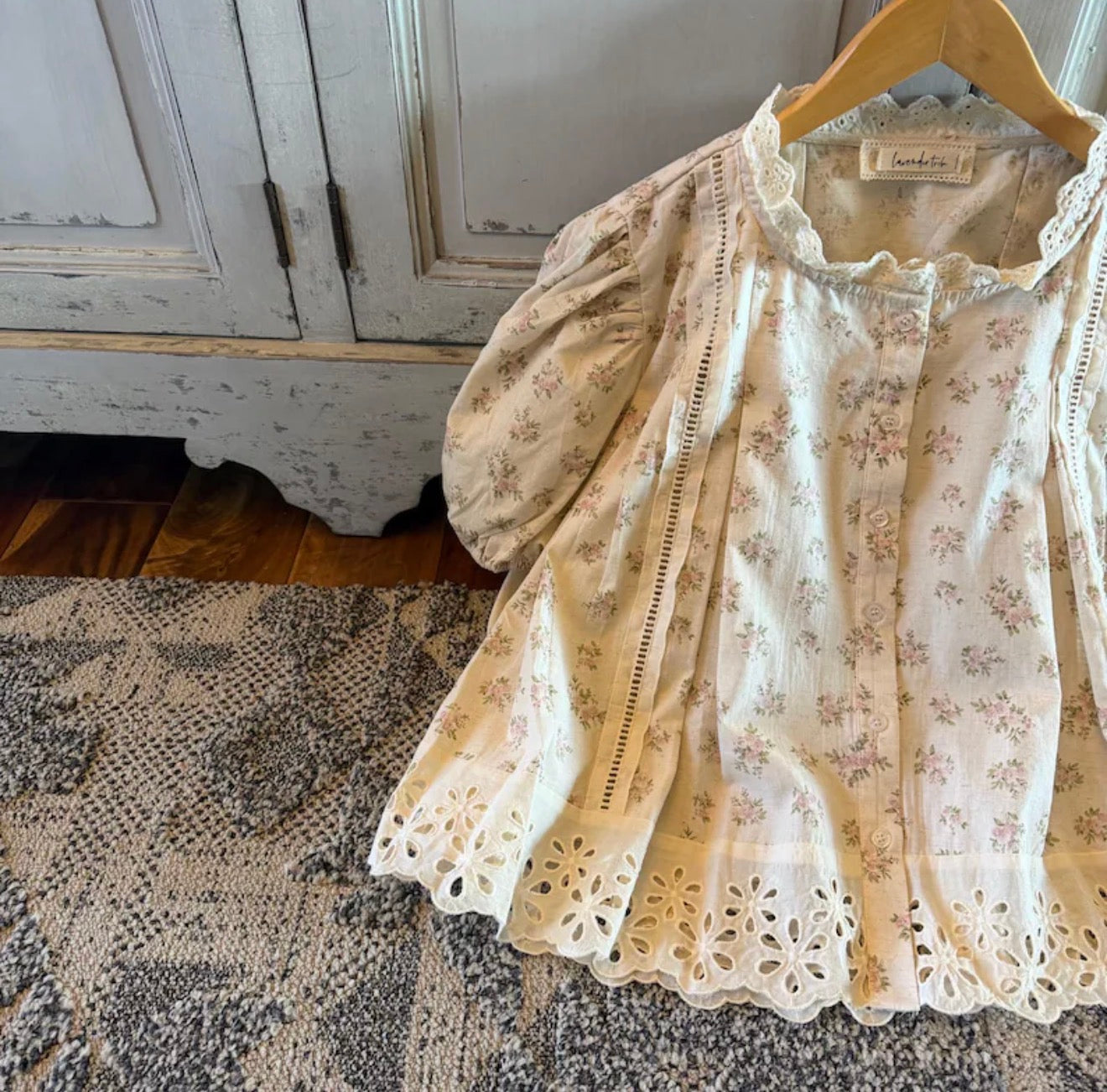 Floral lace top on a hanger against a rustic wooden cabinet background