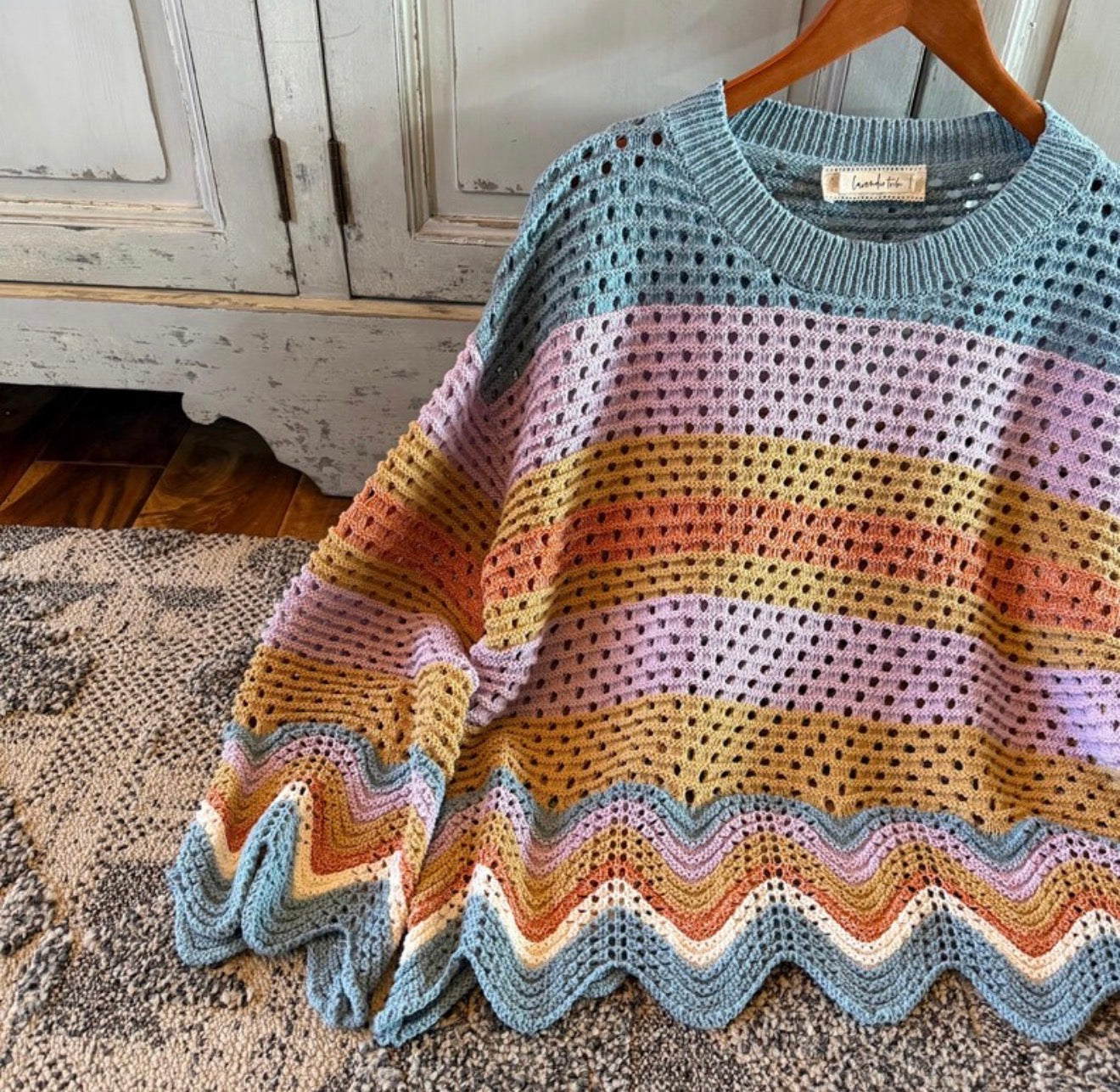Colorful crocheted sweater on a wooden hanger against a rustic background