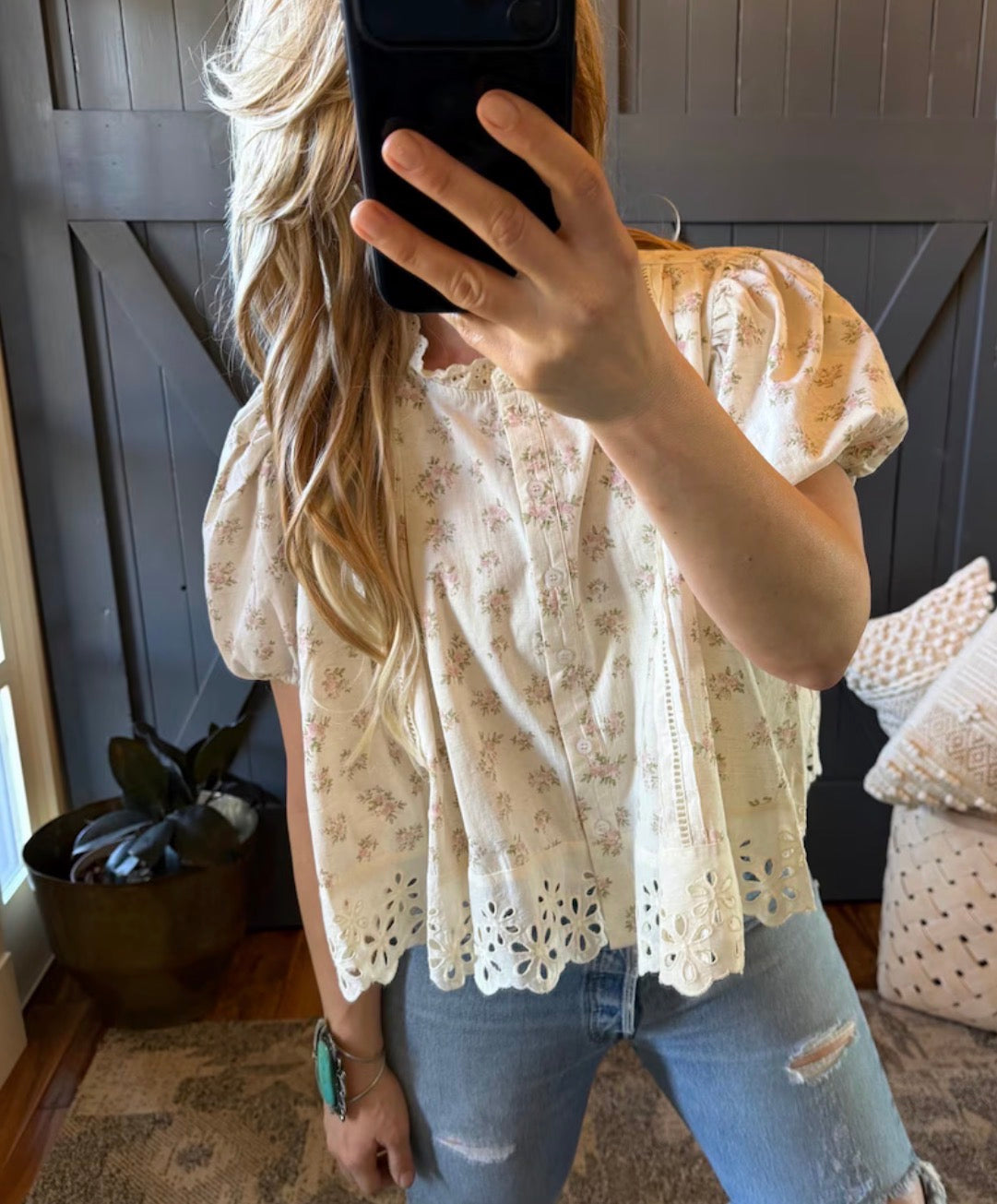 Person wearing a floral blouse and ripped jeans taking a mirror selfie.
