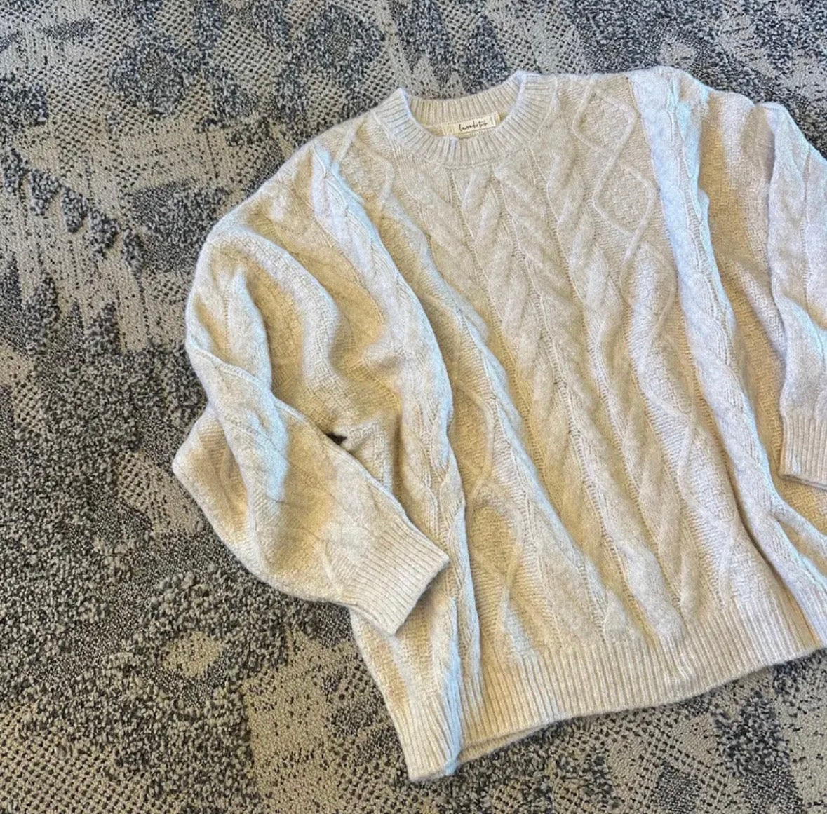 Beige cable knit sweater on a textured surface