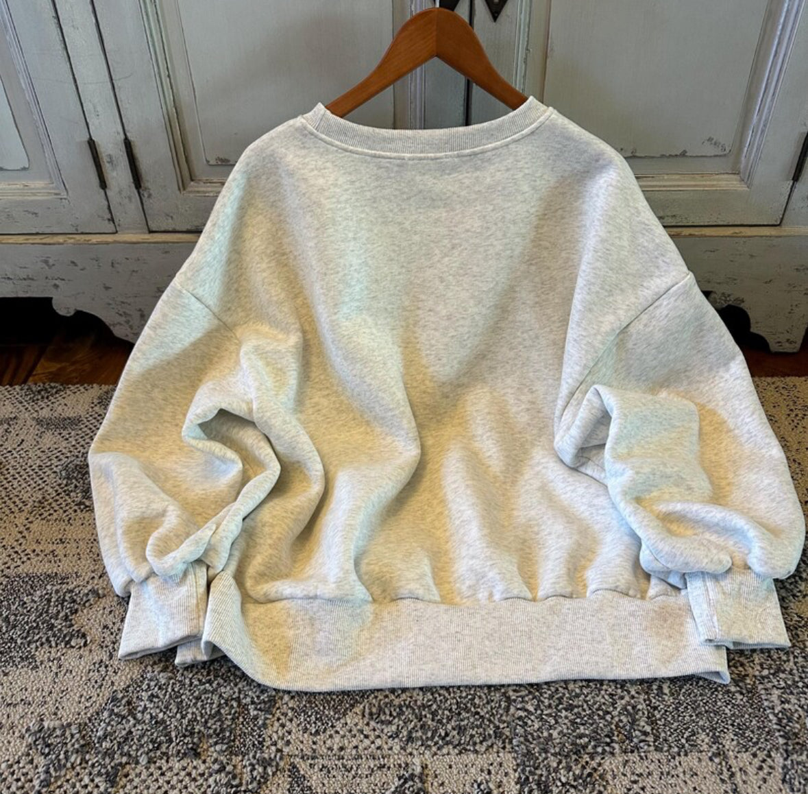 Light-colored sweatshirt on a wooden hanger against a neutral background