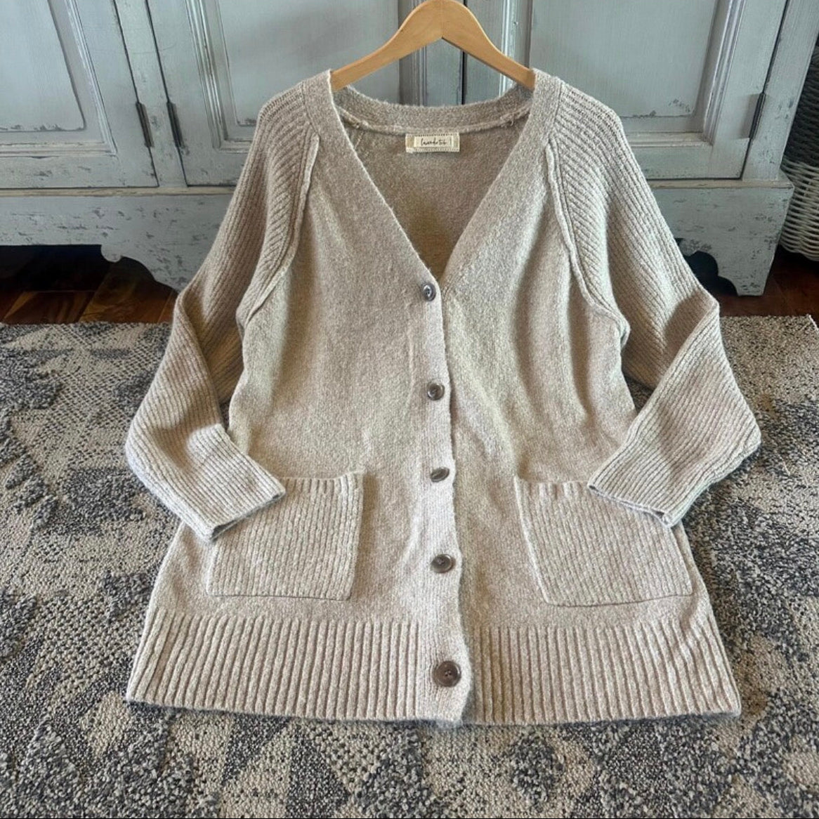 Beige cardigan on a wooden hanger against a rustic background