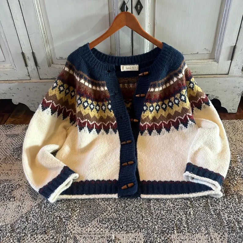 Knitted cardigan with patterned design on a wooden hanger against a rustic wooden door background.