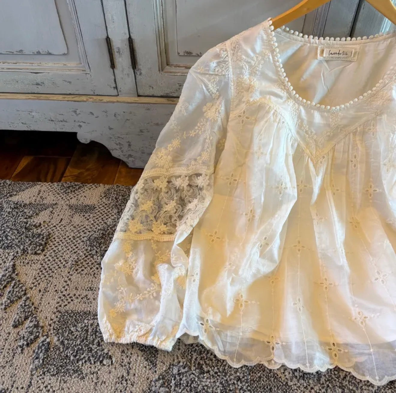 White lace top on a hanger against a neutral background