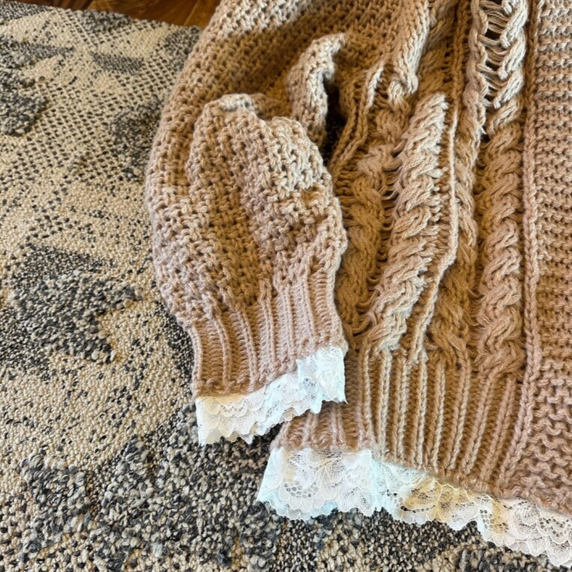 Knitted brown sweater with lace trim on a textured surface