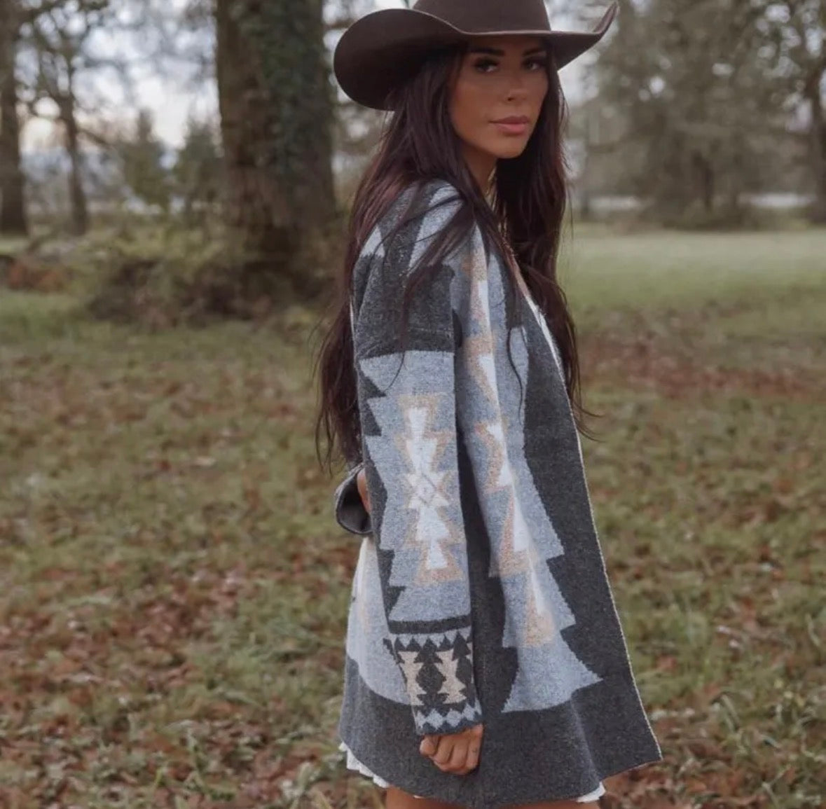 Woman wearing a patterned cardigan and cowboy hat in a natural setting