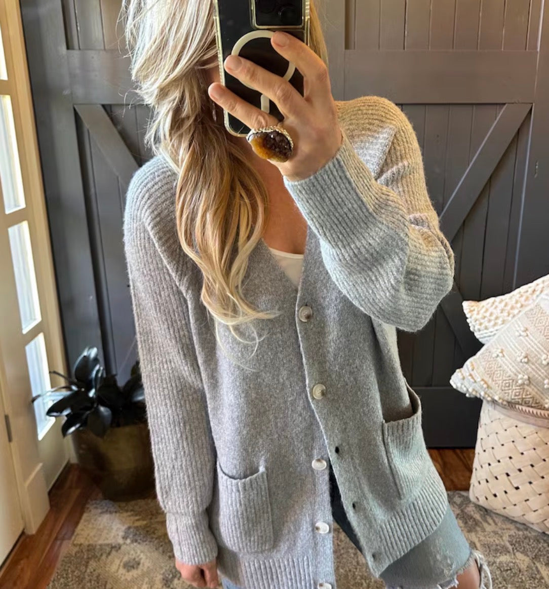 Person wearing a gray cardigan taking a mirror selfie in a home setting.