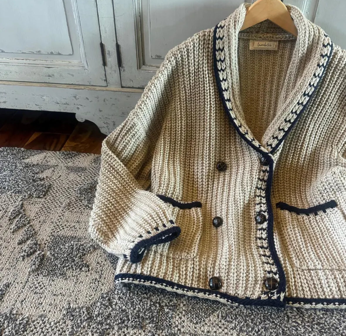 Knitted cardigan with black accents on a wooden hanger against a neutral background