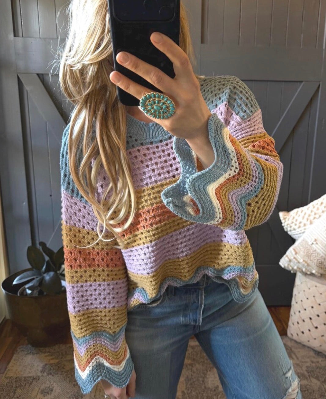 Person wearing a colorful crochet sweater taking a mirror selfie.